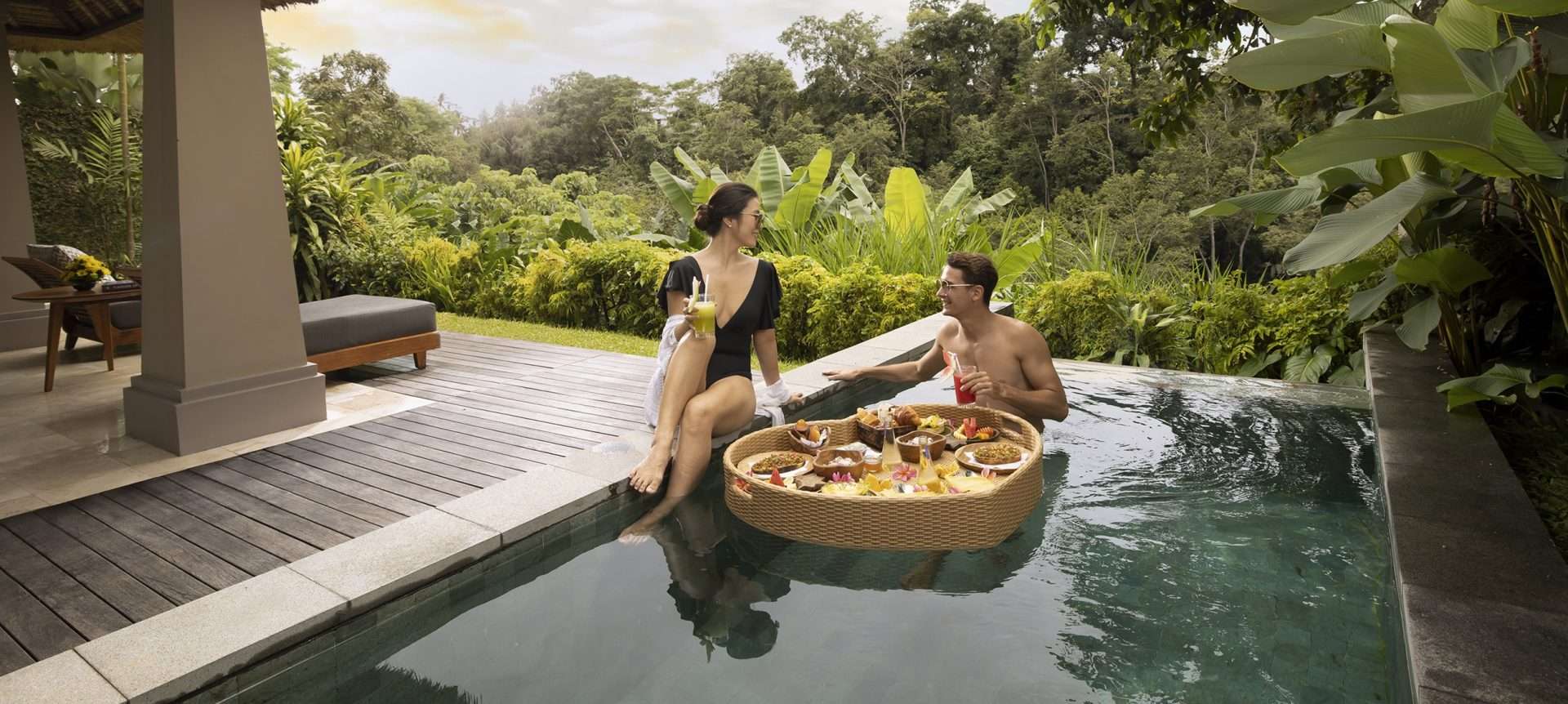 Man and woman having breakfast in the pool with a floating basket of food.